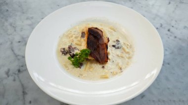 Rigatoni Carbonara Pastırması ve yanında kremalı beyaz sos ve mermer masa.