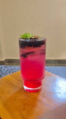 Ahududu ve hindistan cevizi suyu karışımını çimen jölesi ve turunçgil garnitürle ahşap bir masa üzerinde dokulu, şeffaf bir cam ile tazeliyorum.