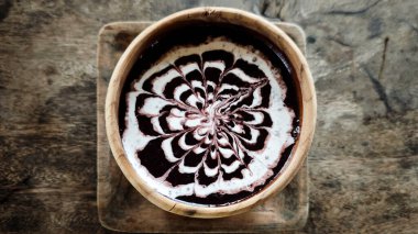 Karmaşık hindistan cevizi sütü sanatı serpiştirilmiş siyah glüten pirinç lapası geleneksel Endonezya tatlı deneyimi için ahşap dokulu bir yüzey üzerinde ahşap bir kasede servis edilir..