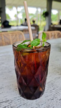 Buzlu siyah çayı dokuma bardakta naneli garnitürle ferahlatıyor. Kırsal bir kafeteryada, rahatlatıcı bir içecek molası için kağıt kamışla servis ediliyor.