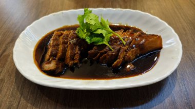 Lokantadaki Ahşap Masa Arkaplanlı Beyaz Tabakta Taze Cilantro ile süslenmiş Koyu Soya Sosu ile kavurulmuş Domuz eti.