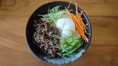 Siyah seramik bir kase karamelli sığır eti susamlı rafadan yumurta ve pirinçli taze jülyen sebzesi kırsal ahşap bir masada.