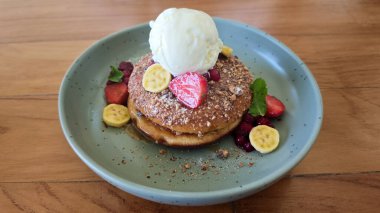 Vanilyalı krep, çilek, muz, kırmızı böğürtlen, nane ve ahşap bir masanın üzerinde pastel yeşil bir tabakta ezilmiş fındık..