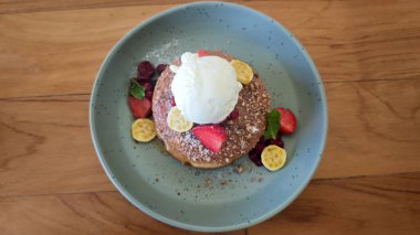 Vanilyalı krep, çilek, muz, kırmızı böğürtlen, nane ve ahşap bir masanın üzerinde pastel yeşil bir tabakta ezilmiş fındık..