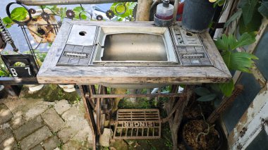 Creative outdoor hand wash station made from a repurposed retro television panel and vintage sewing machine base with a rustic wooden frame in a garden setting with plants and metal decorations clipart