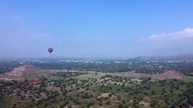 Meksika 'daki Teotihuacan Piramitleri üzerinde güneşin doğuşunu gösteren sıcak hava balonu manzarası.