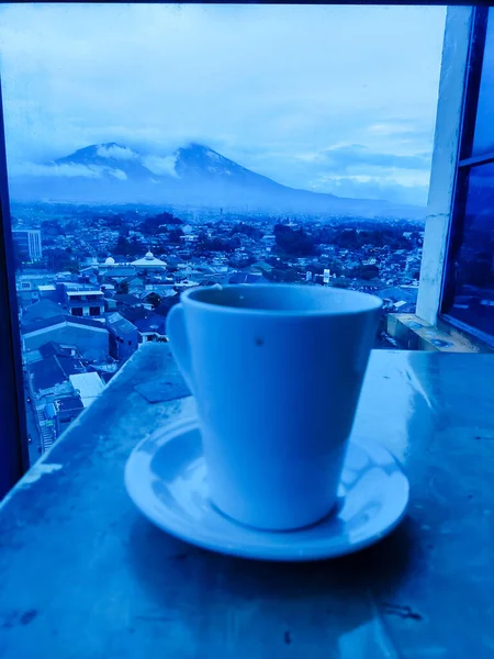 A cup of coffee with the evening city in the background.