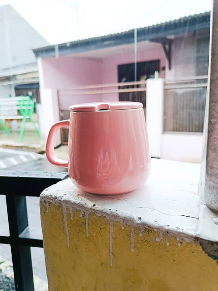 a pink mug with lid on the brick fence