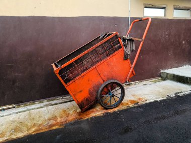 an orange trash cart parking near the red wall