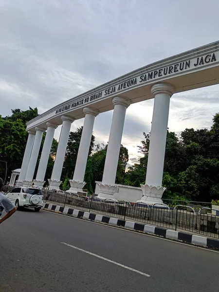 The white pillars in the side of road with Sundanese writing.