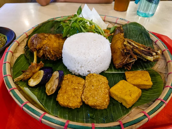 lead rice with fried tempeh and chicken with vegetables on the banana leaves.