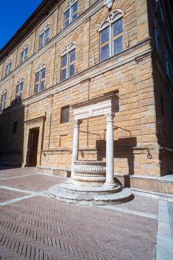 Pienza, Toskana - Piazza Pio II 'deki Palazzo Piccolomini. Ön planda, antik taş ve beyaz mermer kuyu.