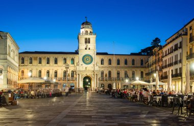 Padua, İtalya - 1 Ekim 2023: Piazza dei Signori veya Piazza della Signoria in the evening. Meydana ünlü Saat Kulesi hükmediyor. Bardaki masalarda oturan ya da etrafta dolaşan insanlar.