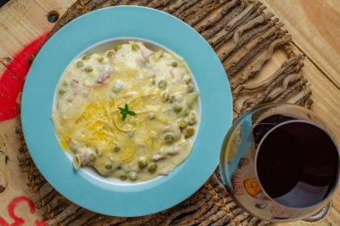 beyaz soslu makarna ve bezelye ve tahta masada bir bardak kırmızı şarap.