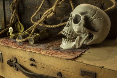 Kafatası antik seyahat çantaları ve macera eşyaları, dürbün, pusula, ip ve parşömenlerin yanında..