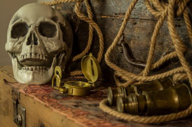 Kafatası antik seyahat çantaları ve macera eşyaları, dürbün, pusula, ip ve parşömenlerin yanında..