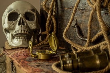 Kafatası antik seyahat çantaları ve macera eşyaları, dürbün, pusula, ip ve parşömenlerin yanında..