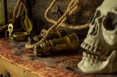 Kafatası antik seyahat çantaları ve macera eşyaları, dürbün, pusula, ip ve parşömenlerin yanında..