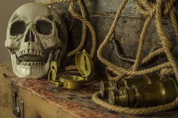 Kafatası antik seyahat çantaları ve macera eşyaları, dürbün, pusula, ip ve parşömenlerin yanında..