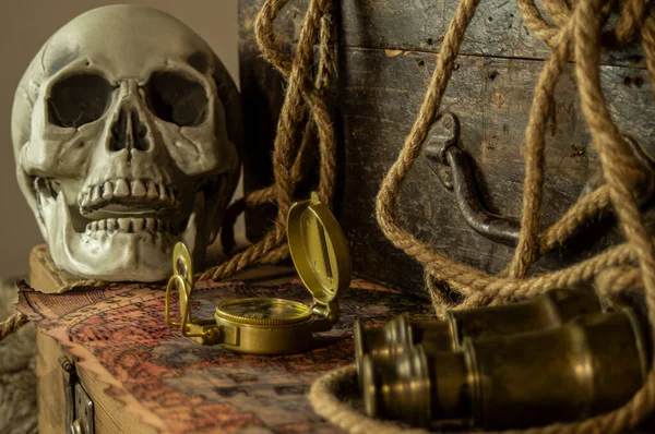 Kafatası antik seyahat çantaları ve macera eşyaları, dürbün, pusula, ip ve parşömenlerin yanında..