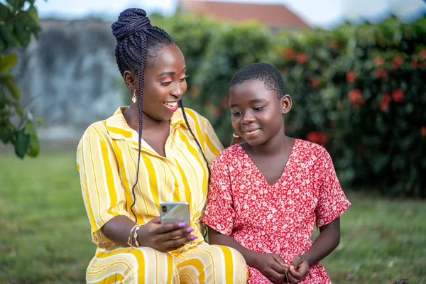 Beautiful image of African lady holding smart phone and a kid besides her- seated black people enjoying social media surf