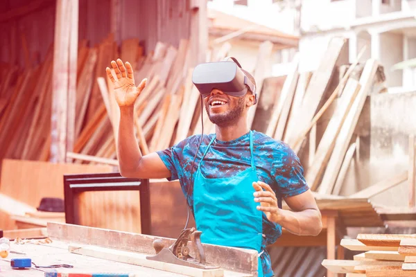 smiling bearded young man using virtual reality headset -filtered image of african guy with eye wear gadget in local workshop- technology concept