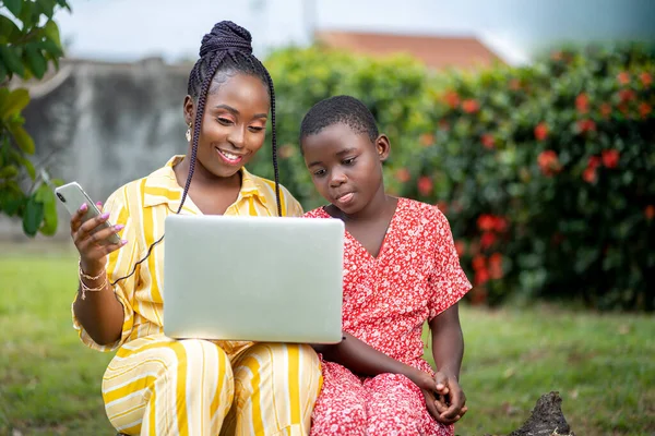 Beautiful image of African lady holding laptop and a kid besides her- seated black people enjoying social media surf