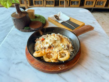 Pirinç, sebze ve etle dolu tava yemeği kremalı sos veya satranç peyniri sosu ve mermer bir yüzeye yerleştirilmiş gevrek soğan halkaları ile kaplı. Lezzetli ve sağlıklı bir yemeğe benziyor.