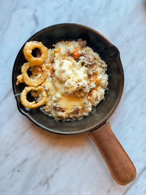 Pirinç, sebze ve etle dolu tava yemeği kremalı sos veya satranç peyniri sosu ve mermer bir yüzeye yerleştirilmiş gevrek soğan halkaları ile kaplı. Lezzetli ve sağlıklı bir yemeğe benziyor.