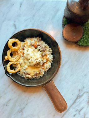 Pirinç, sebze ve etle dolu tava yemeği kremalı sos veya satranç peyniri sosu ve mermer bir yüzeye yerleştirilmiş gevrek soğan halkaları ile kaplı. Lezzetli ve sağlıklı bir yemeğe benziyor.