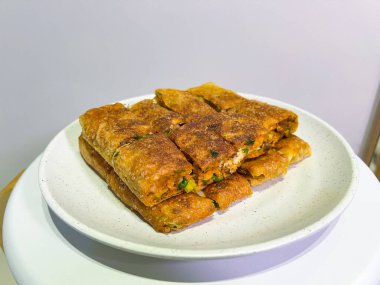 Geleneksel bir Endonezya sokak yemeği olan altın-kahverengi martabak telur tabağı beyaz bir tabakta sunulmaktadır. Her dilim lezzetli bir yumurta, et, soğan ve diğer malzemeleri ortaya çıkarıyor.