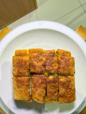 Geleneksel bir Endonezya sokak yemeği olan altın-kahverengi martabak telur tabağı beyaz bir tabakta sunulmaktadır. Her dilim lezzetli bir yumurta, et, soğan ve diğer malzemeleri ortaya çıkarıyor.