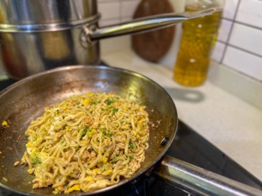 Ağzına kadar lezzetli eriştelerle dolu büyük bir tava aktif olarak sıcak bir sobada pişiyor ve mutfak havasına baştan çıkarıcı kokular yayıyor.