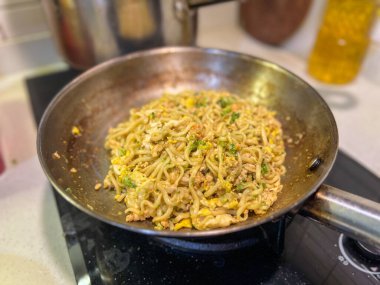 Ağzına kadar lezzetli eriştelerle dolu büyük bir tava aktif olarak sıcak bir sobada pişiyor ve mutfak havasına baştan çıkarıcı kokular yayıyor.