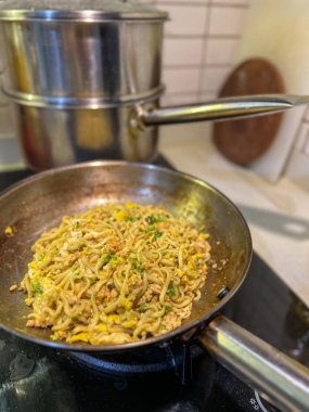 Ağzına kadar lezzetli eriştelerle dolu büyük bir tava aktif olarak sıcak bir sobada pişiyor ve mutfak havasına baştan çıkarıcı kokular yayıyor.