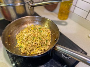 Ağzına kadar lezzetli eriştelerle dolu büyük bir tava aktif olarak sıcak bir sobada pişiyor ve mutfak havasına baştan çıkarıcı kokular yayıyor.