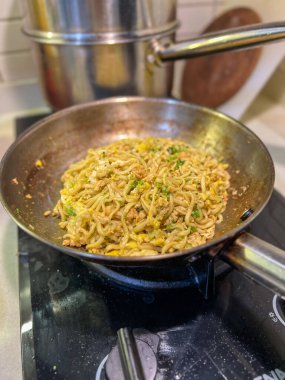 Ağzına kadar lezzetli eriştelerle dolu büyük bir tava aktif olarak sıcak bir sobada pişiyor ve mutfak havasına baştan çıkarıcı kokular yayıyor.