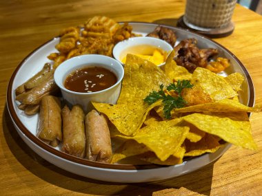 Nacholar, börekler, cipsler, sosisler ve çeşitli sosisler içeren canlı bir aperatif tabağı..