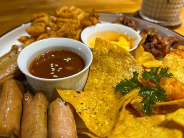 Nacholar, börekler, cipsler, sosisler ve çeşitli sosisler içeren canlı bir aperatif tabağı..