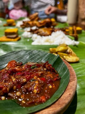 Muz yaprakları üzerinde geleneksel yemeklerin canlı bir sunumu, baharatlı acı biber sosu ve çeşitli eşliklerle, zengin mutfak mirası sergileniyor..