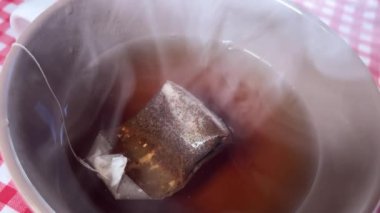 Fincanda sıcak su bulunan çay poşeti ağır çekimde buhar üretiyor.