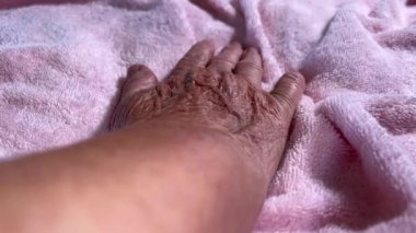 Yatakta dinlenen yaşlı bir kadının kırışık eli.