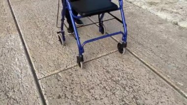 Elderly woman walks with walker on the concrete brick road