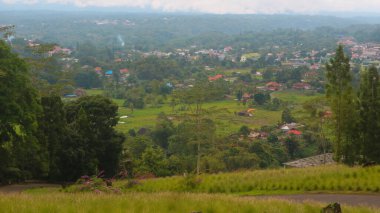 Bulutlu gökyüzü, ağaçlar, dağlar ve tepeden çekilen evler.