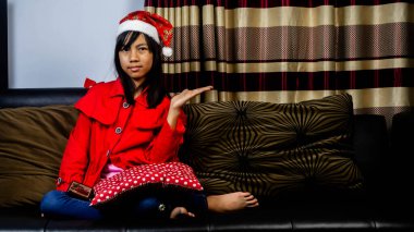 Noel Baba kıyafeti giyen küçük kız siyah bir koltukta oturuyor.