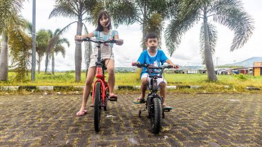 Çocuklar güzel bir bahçede bisiklet oynuyorlar.