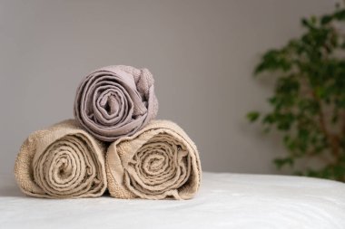 Masaj masasında üç bükülmüş havluyla bir spa salonunda ışık duvarı ve yeşil bitkilerin olduğu bir kompozisyonun yakın çekimi. Boşluğu kopyala
