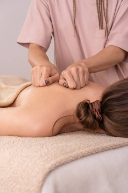 Kadın masör, yumuşak ışıklandırmalı, yakın plan bir kaplıcada genç bir kadının sırt ve omuz ve omuzlarına masaj yapıyor. Vücut bakımı, sağlık, masaj spa tedavileri kavramı. Dikey fotoğraf