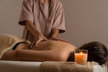 Kadın masör, yanan mumlarla bir kaplıca salonunda rahatlatıcı bir sırt masajı yapıyor. Sağlık kavramı, vücut bakımı