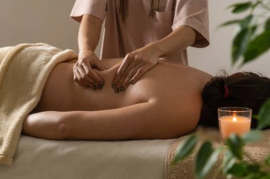 Masör, spa salonunun rahat atmosferinde yeşil bitkilerle, yanan bir mumla sırt masajı yapıyor. Sağlıklı yaşam tarzı ve vücut bakımı kavramı.